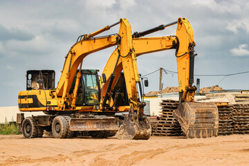 Fototapeta premium Powerful excavators at a construction site against a blue cloudy sky. Earthmoving construction equipment. Lots of excavators.