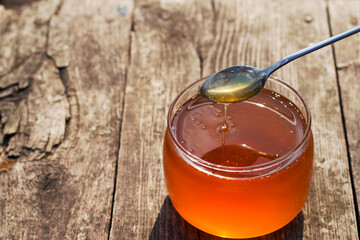 fresh golden honey in a glass jar with a spooon on wooden table