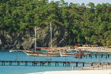Fototapeta na wymiar Recreational yacht standing in the bay at the pier in the resort area. Narrow Mediterranean bay with pebble beach with pier and parked yacht