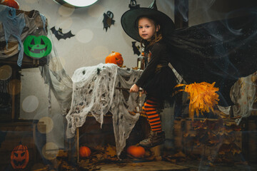 Little girl 3-4 years old in witch costume and striped stockings flies on broom in Halloween yard...