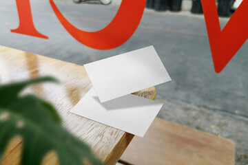 Clean minimal business card mockup floating on top wood in cafe and leaves