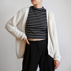 Woman wearing white chunky cardigan, striped t shirt and black trousers isolated on white background.