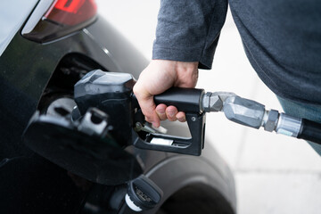 Man at gas station pumping fuel into car petrol tank, close up of hand, arm, nozzle and open tank of passenger vehicle which produces environmentally harmful carbon dioxide CO2 emissions - 530873297