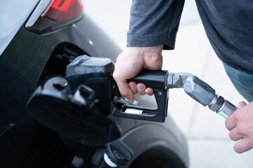 Man at gas station pumps regular, expensive fossil fuel with nozzle into passenger car with environmentally unfriendly combustion engine producing carbon dioxide CO2 emissions - 530873298