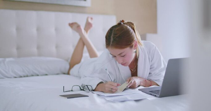 Young lady doing homework assignment lying on bed with netbook