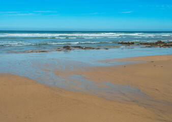 Fototapeta na wymiar View of empty Praia do Queimado beach with ocean waves and sharp rocks and wet golden sand at wild Rota Vicentina coast near Porto Covo, Portugal.