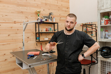Handsome male groomer with professional equipment on his workplace in grooming salon for pet