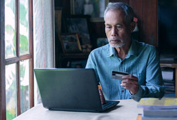 Asian old man using laptop and credit card payment online shopping by connecting customer network through omni channel old man with technology