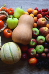 Round straw bag and various healthy fruits and vegetables on wooden background.