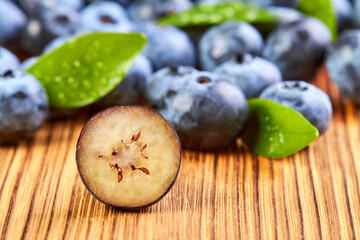 Close-up of a Cut half blueberry on a wooden surface against a background of blueberries with green leaves