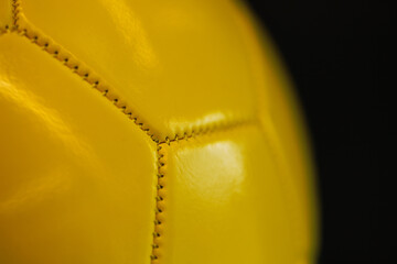 Close-up of the seams of a yellow sports ball on a dark background