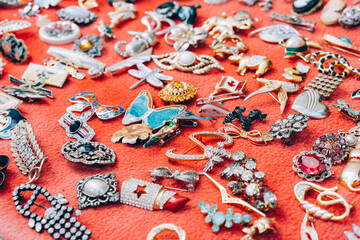 Vintage brooches, pins and badges at flea market stall or car boot sale over red background. Vintage goods for sale. Garage sale concept. Selective focus