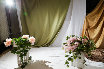 Bouquets of flowers standing on white wooden boxes standing in studio with white and green curtains in the background