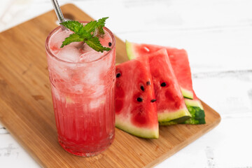 Watermelon smoothie or iced juice with watermelon slices and mint leaf on a white wooden background