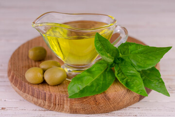 Olive oil in a gravy boat on a wooden board and basil leaves.	