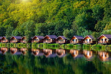 Obraz premium Wooden houses on the water near the forest for carp fishing. A place to relax in nature. Autumn carp fishing season.