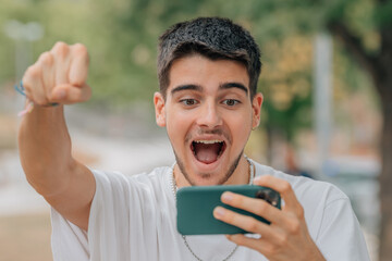 excited young man playing or looking at mobile phone
