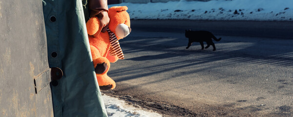 Soldier or rescuer wearing chemical clothes holds plush bear in hand against black cat walking at street
