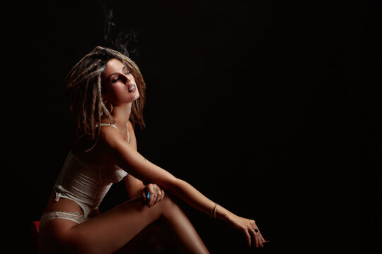 Portrait of a seated young woman, wearing dreadlocks, smoking a cigarette