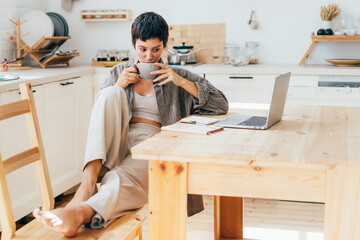Young woman drinking coffee has a break while working on computer gadgets. - obrazy, fototapety, plakaty