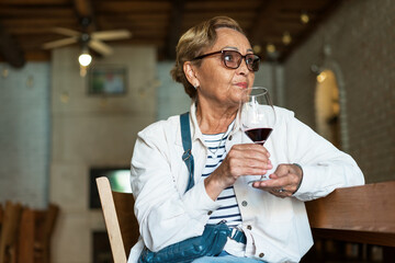 Casual clothing elderly woman 65 years old tasting wine in a winery.