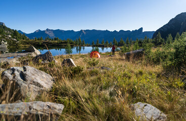 Hiker beside her red tent in the mountains of Ticino on a beautiful morning in the summer.