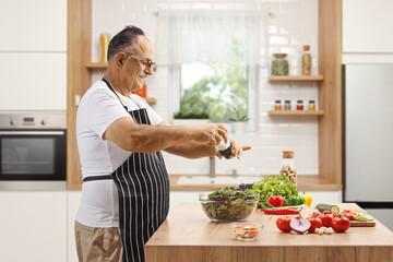 Mature man seasoning a salad on a kitchen counter