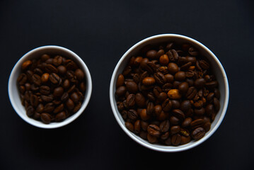 Delicious coffee beans in a ceramic white bowl on a black background. Coffee beans close-up in the dishes.