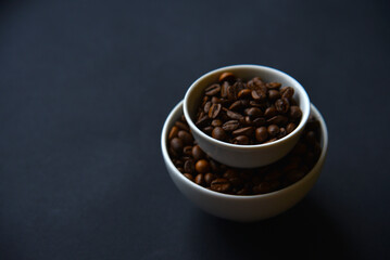 Delicious coffee beans in a ceramic white bowl on a black background. Coffee beans close-up in the dishes.