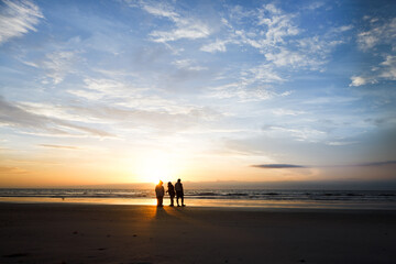 Silhouetted group of people walking down the beach during sunrise