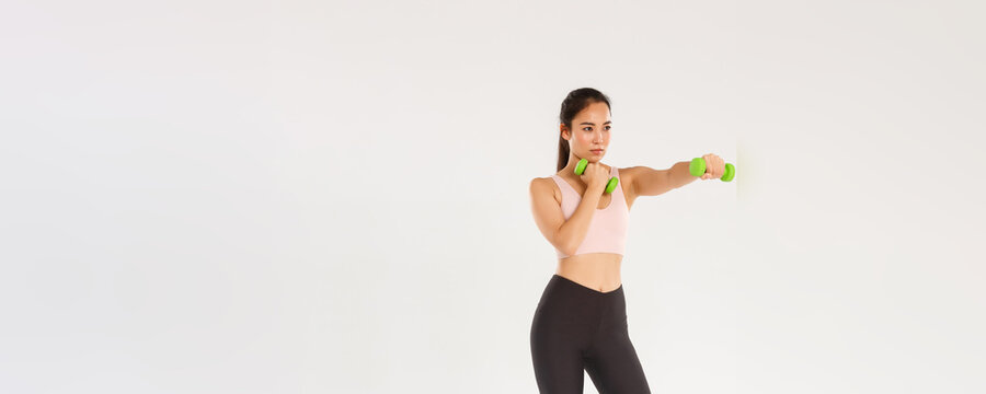 Sport, Gym And Healthy Body Concept. Full Length Of Focused Female Athelte, Asian Brunette Girl Doing Fitness Exercises, Workout With Dumbbells, Practice Shadowboxing Over White Background