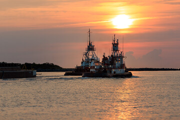 Obraz premium Tow Boats towing cargo through the port during sunrise. 