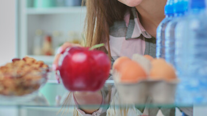 Portrait of female standing near open fridge full of healthy food, vegetables and fruits.