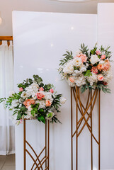 Beautiful multi-colored flowers stand on a bronze stand against a white wall in a restaurant, interior. Wedding decorations, photography.