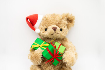 A stuffed toy Teddy bear in a red Santa Claus hat with a pompom on ear, holding green gift boxes in its paws. The concept of Christmas gifts, sales