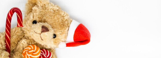 Banner with stuffed toy Teddy bear in a red Santa Claus hat on one ear, holding candy cane and two striped lollipops in its paws. Concept of Christmas © Yulia