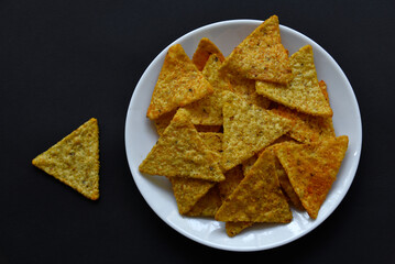Mexican nachos corn chips with pepper on a white plate on a black background. Delicious breakfast of peppered nachos.