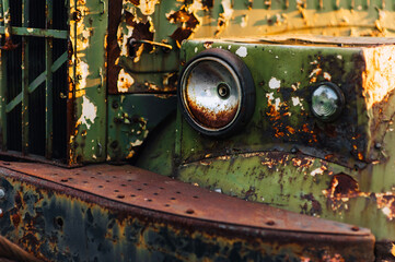 The front end with the headlight of an old, rusty truck car with cracked paint.