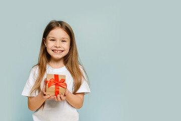 Little girl holding a gift on a blue background with copy space. Looking at camera