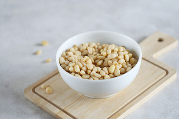 Peeled pine nuts lie in a plate on a wooden board. Selective focus, copy space