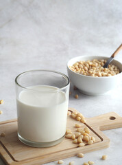 A glass of cedar milk stands on a wooden board on a concrete table. Pine nuts are scattered nearby, and a bowl of pine nuts is behind.