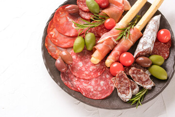 Charcuterie plate with variery of sausages - salami, bresaola, proscuitto served with olives and grissini on white table. Menu background with copy space. Traditional italian food - antipasti