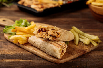 Chicken Wrap shawarma with fries served in a cutting board isolated on wooden table background side view of fastfood