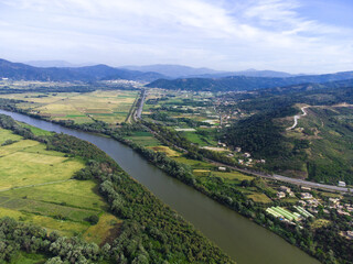 Fototapeta na wymiar Aerial View of green and yellow agricultural fields, plains with a river in the middle, mountains and cloudy sky in the background, Aerial view of bright river flowing through green meadows, Algeria