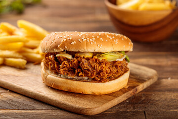 Chicken zinger burger with french fries served in a cutting board isolated on wooden table...