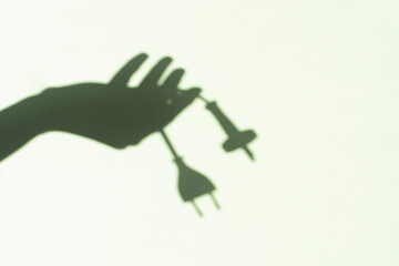 Shadow of woman hand holding electric power cords with plugs on wall background. Electric power wire with European plug. Saving of electricity, expensive electricity concept