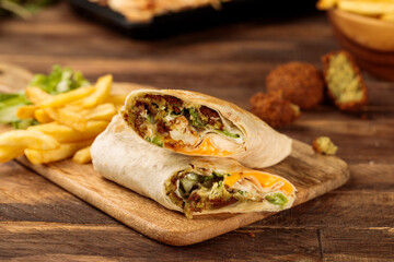 Falafel wrap shawarma with fries served in a cutting board isolated on wooden table background side...