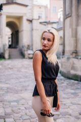 A young, blonde girl in a black blouse and sunglasses poses against the backdrop of an old courtyard in Lviv. Ukraine.