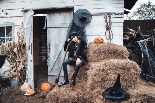 Beautiful scary little girl celebrating halloween. Terrifying black, white half-face makeup,witch costume, stylish image. Fun at children's party in barn on street. Hat,jacket, pumpkin jack-o-lantern