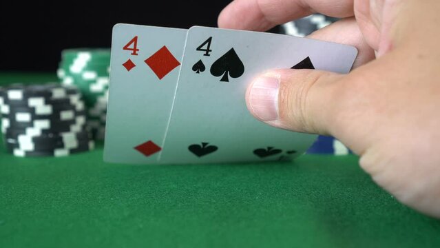 Poker game with a pair of fours betting all the poker chips. Close-up of a gambler hand is holding playing cards in poker club